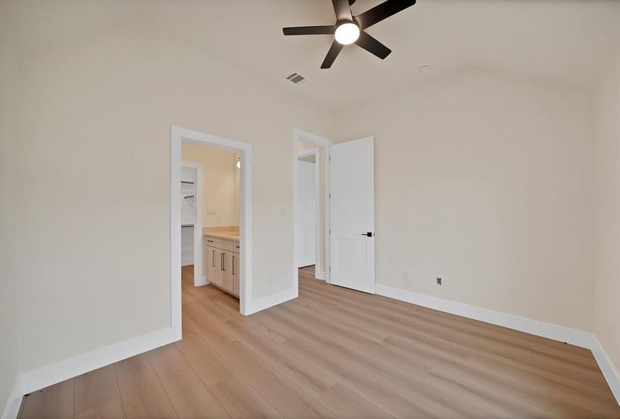 Unfurnished bedroom featuring light wood finished floors, connected bathroom, ceiling fan, and a spacious closet Unfurnished bedroom featuring light wood finished floors, connected bathroom, ceiling fan, and a spacious closet