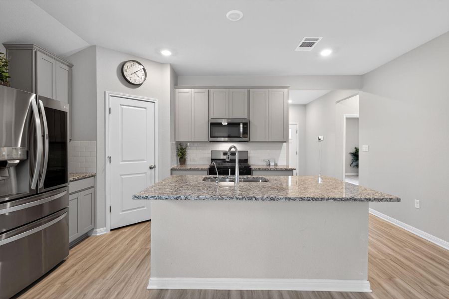 Kitchen featuring gray cabinetry, stainless steel appliances, light stone countertops, a center island with sink, and light wood-style floors