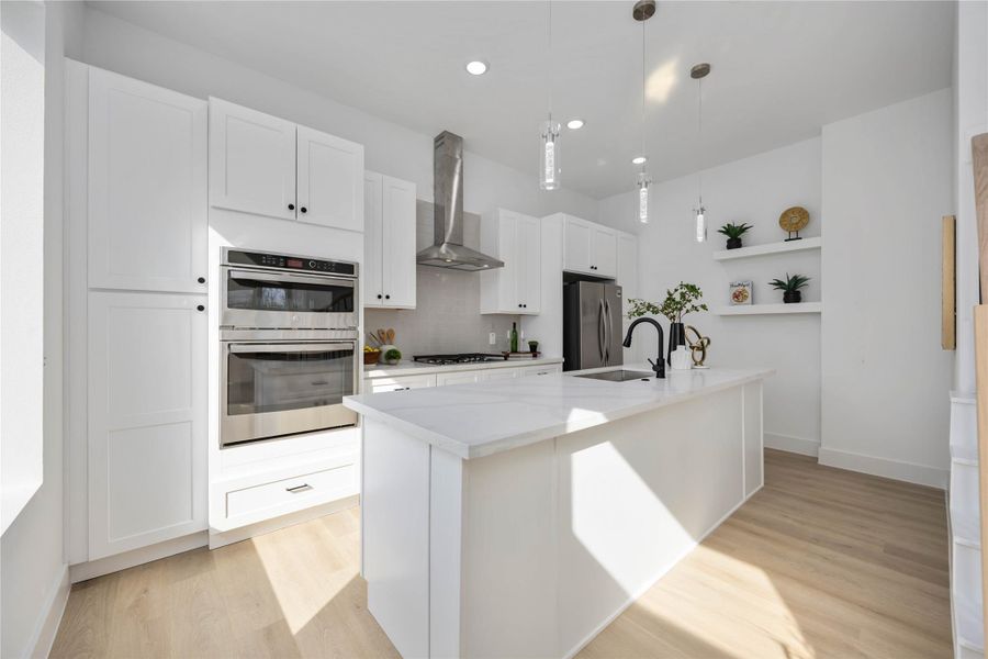 A bright, modern kitchen features sleek white cabinetry, polished white quartz countertops, a stylish glossy subway-tile backsplash, stainless steel appliances, and a spacious waterfall-edge kitchen island accented by a matte black faucet and pendant lighting.
