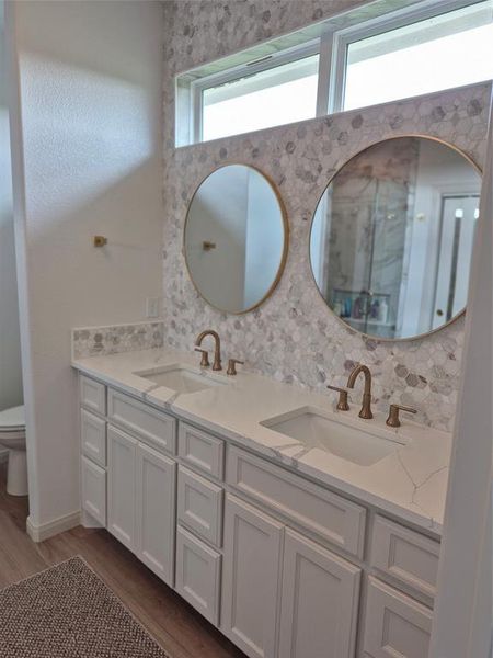 Bathroom with double vanity, dark wood finished floors, backsplash, and a shower with shower door