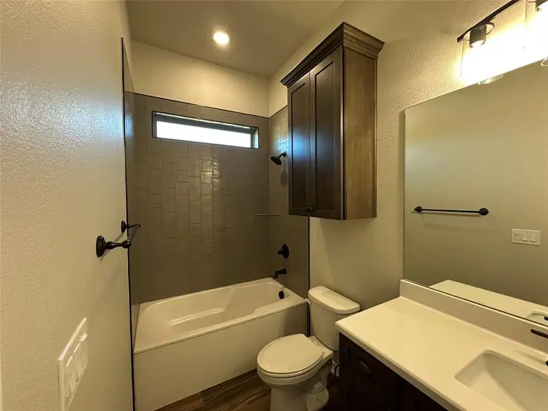 Bathroom featuring a textured wall, shower combination, vanity, and dark wood-type flooring Bathroom featuring a textured wall, shower combination, vanity, and dark wood-type flooring
