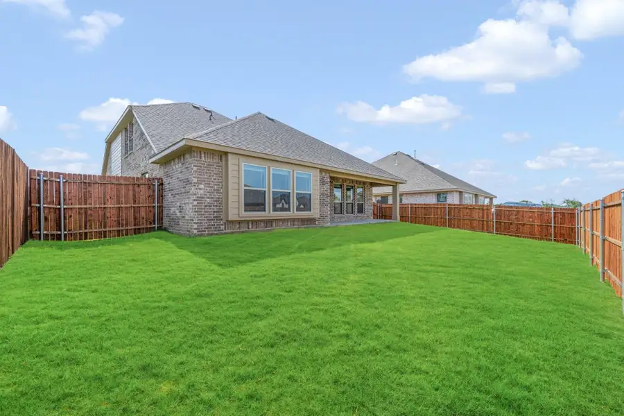 Backyard of brick home with large green lawn, wood privacy fence, and covered patio area