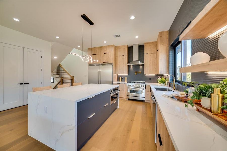 Kitchen with wall chimney range hood, a center island, pendant lighting, premium appliances, and light stone counters