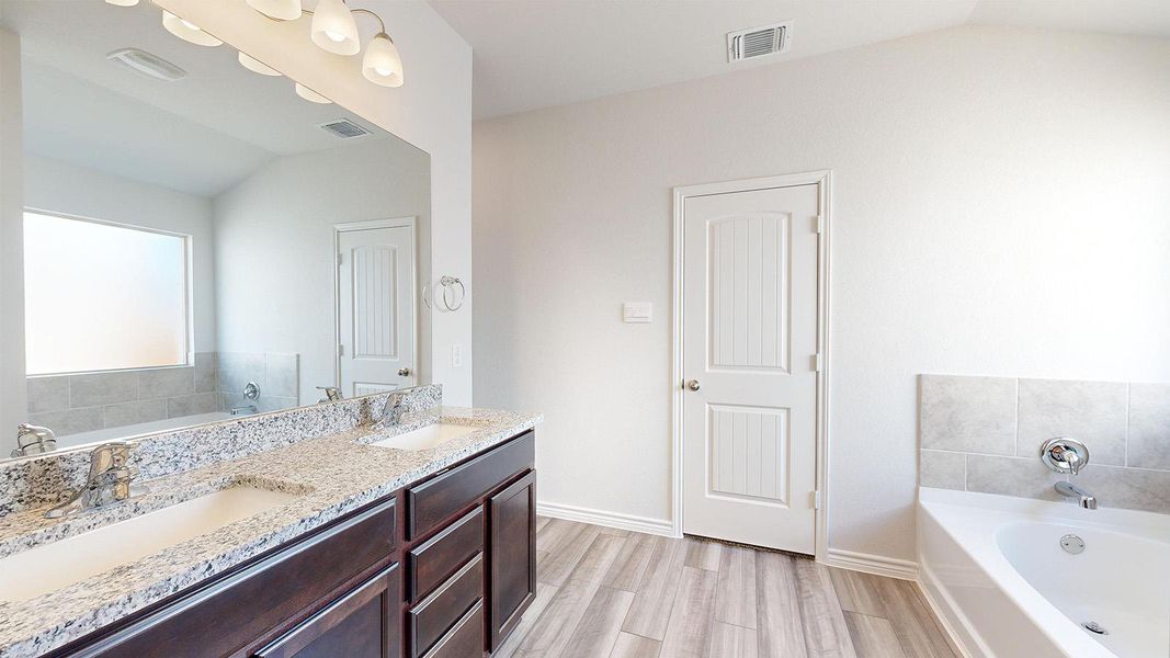 Bathroom featuring a garden tub, lofted ceiling, double vanity, and light wood-style floors Bathroom featuring a garden tub, lofted ceiling, double vanity, and light wood-style floors