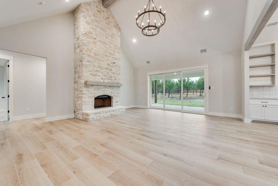 Unfurnished living room featuring beamed ceiling, high vaulted ceiling, a fireplace, a chandelier, and light hardwood / wood-style flooring