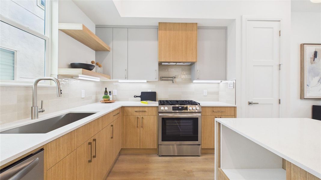 This kitchen features a modern design with light wood cabinets, a sleek stainless steel gas stove, and white countertops. It includes open shelving, ample storage, and under-cabinet lighting, creating a bright and functional space.