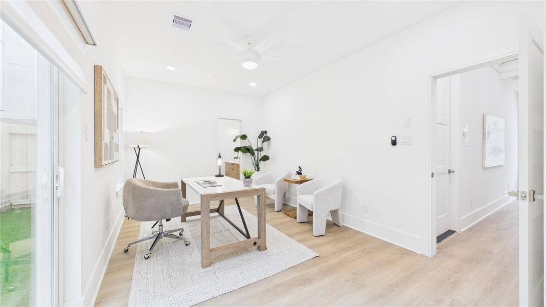 This bright, modern home office features light wood flooring, white walls, and ample natural light from a large sliding glass door. It includes a sleek desk, comfortable seating, and stylish decor, creating a productive and inviting workspace.