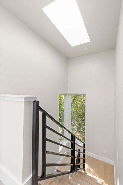Natural light pours through a large overhead skylight illuminating the modern wooden staircase.