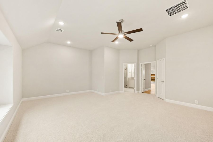 Spacious empty bedroom with vaulted ceiling, ceiling fan, carpet flooring, and doors leading to bathroom and closet. Spacious empty bedroom with vaulted ceiling, ceiling fan, carpet flooring, and doors leading to bathroom and closet.