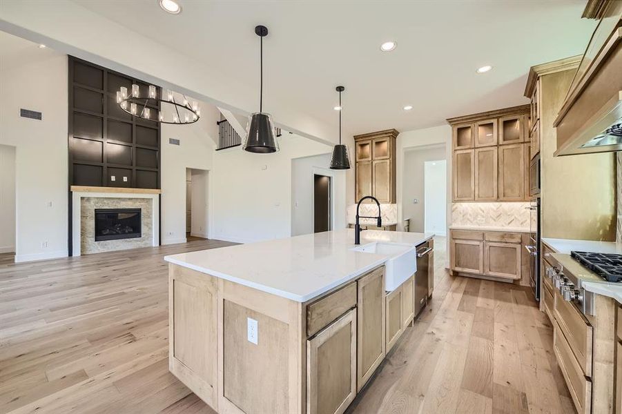 Kitchen featuring sink, light wood-type flooring, hanging light fixtures, a notable chandelier, and a kitchen island with sink