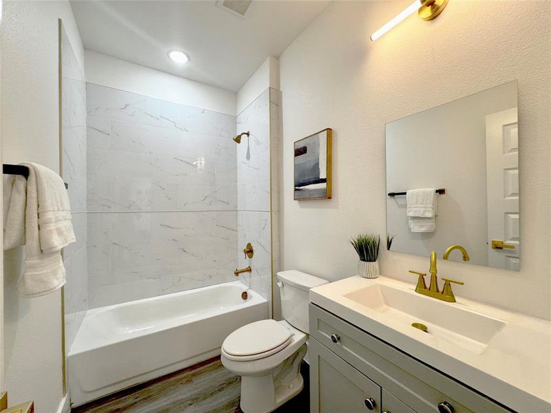 Full bathroom with wood-type flooring, tiled shower / bath, vanity, and toilet