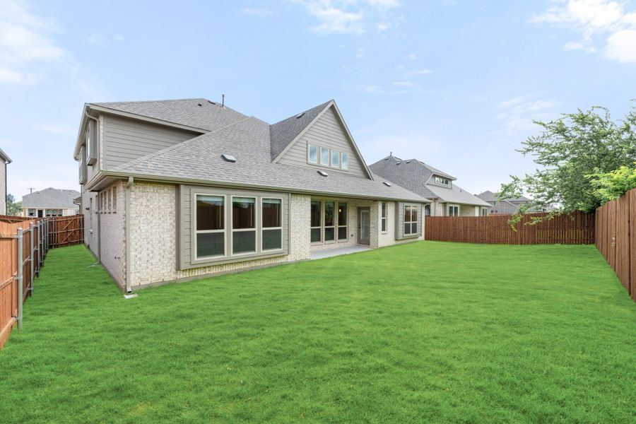 Rear view of two-story brick home with large fenced backyard and green lawn Rear view of two-story brick home with large fenced backyard and green lawn