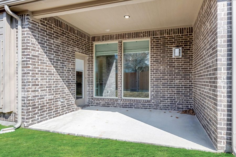 Covered back patio with concrete floor, brick walls, sliding glass door, and small lawn area. Covered back patio with concrete floor, brick walls, sliding glass door, and small lawn area.