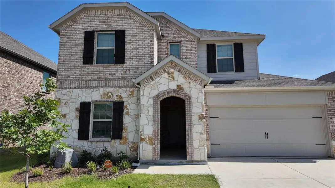 View of front facade featuring stone siding, driveway, and a shingled roof