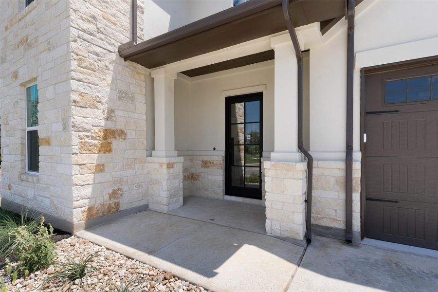 Stone veneer facade with a covered entry, dark-framed glass panel door, and an attached garage featuring a dark wood-finish door