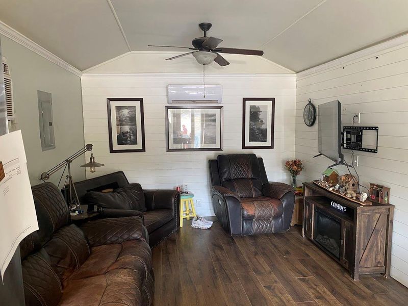 Living room with vaulted ceiling, hardwood / wood-style flooring, ornamental molding, electric panel, and wood walls