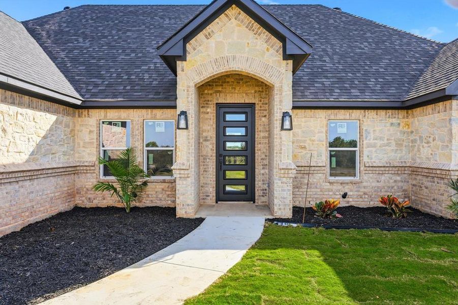 Entrance to property with stone siding, a yard, and a shingled roof