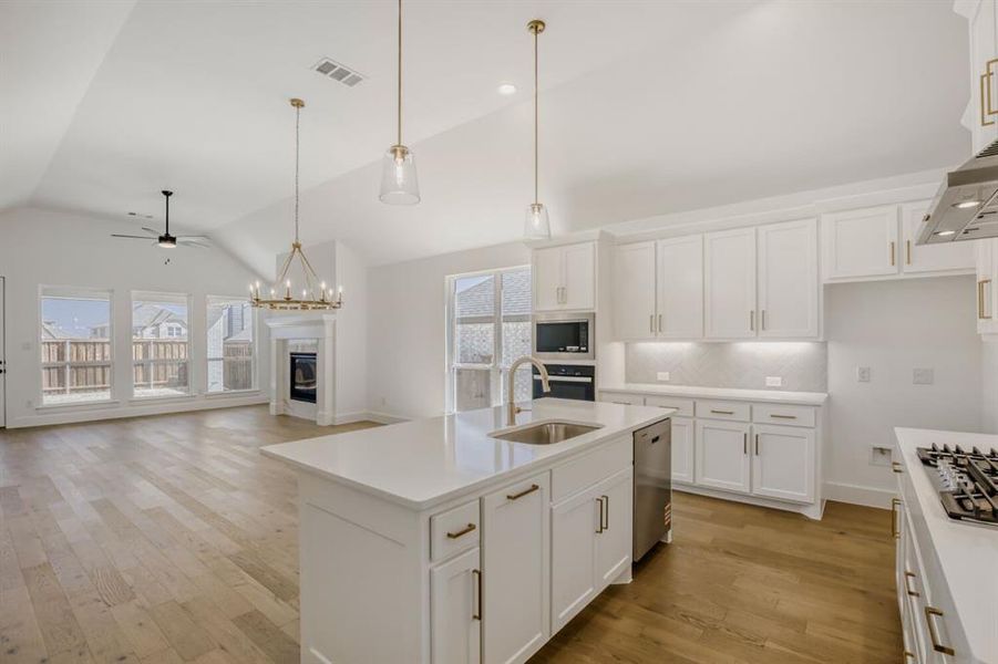 Kitchen featuring white cabinetry, a ceiling fan, a glass covered fireplace, a center island with sink, and a high ceiling