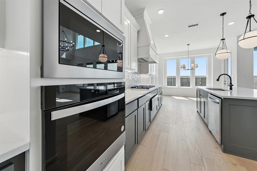 Kitchen featuring appliances with stainless steel finishes, white cabinets, light wood-type flooring, hanging light fixtures, and light stone countertops