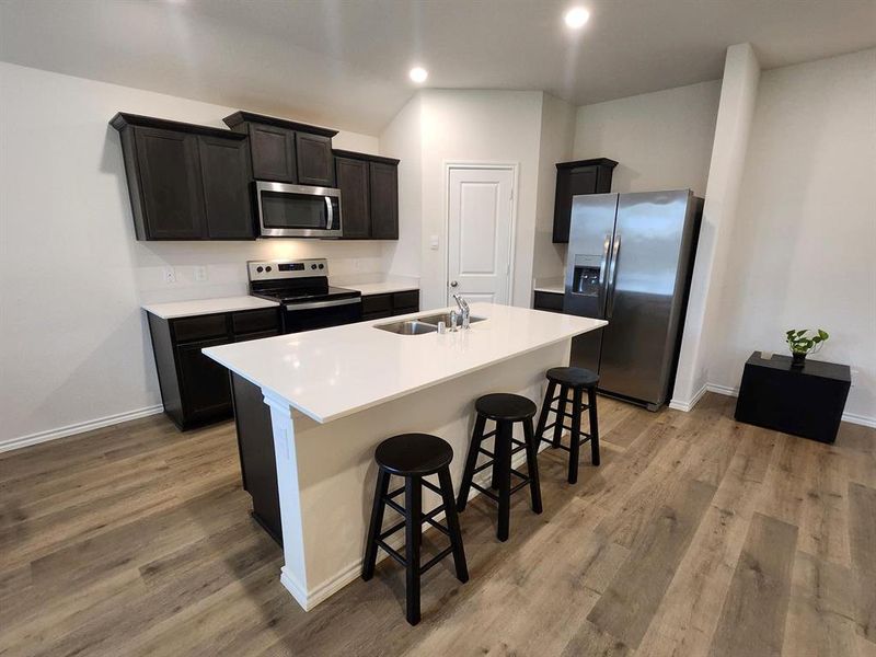 Kitchen featuring fridge, range, a breakfast bar, a center island with sink, and light wood-type flooring