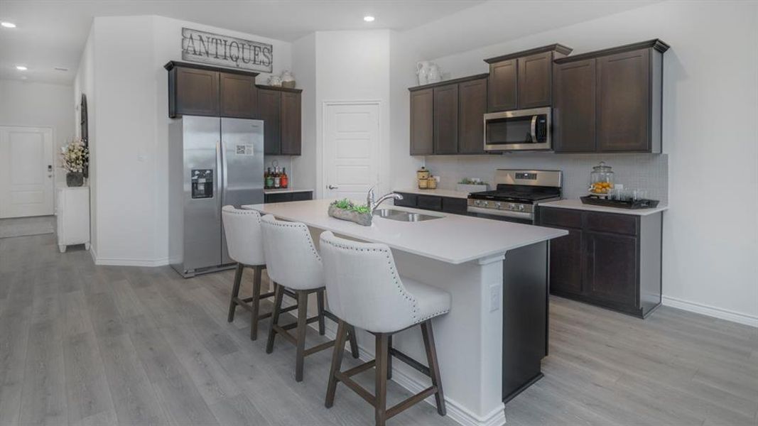 Modern kitchen featuring an island with a breakfast bar, stainless steel appliances, dark wood-finish cabinetry, light countertops, and wood-look flooring