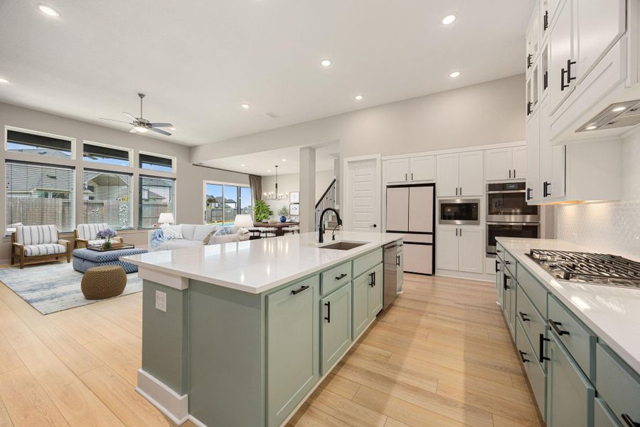 This bright and airy kitchen opens seamlessly to the living and dining areas, creating the perfect flow for everyday living and entertaining. Featuring crisp white cabinetry, a large center island with contrasting tones, and sleek quartz countertops, the space is as functional as it is stylish. Expansive windows in the adjacent living area fill the room with natural light and provide a welcoming view of the backyard.