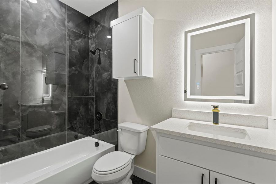 Bathroom featuring a textured wall, shower / bathtub combination, and vanity