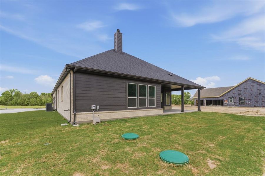 Back of house featuring a yard, a patio, a chimney, and roof with shingles