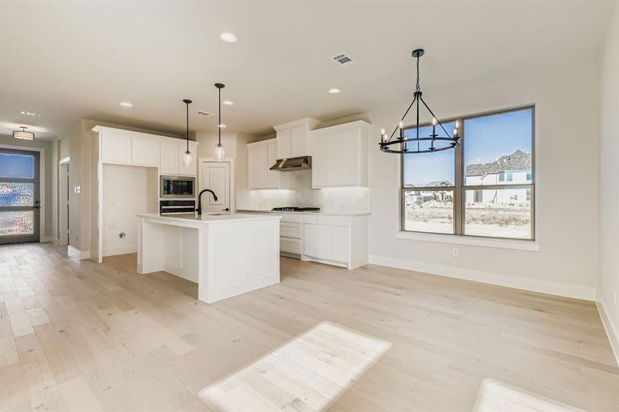 Kitchen featuring healthy amount of natural light, a chandelier, light wood-style flooring, white cabinets, and recessed lighting