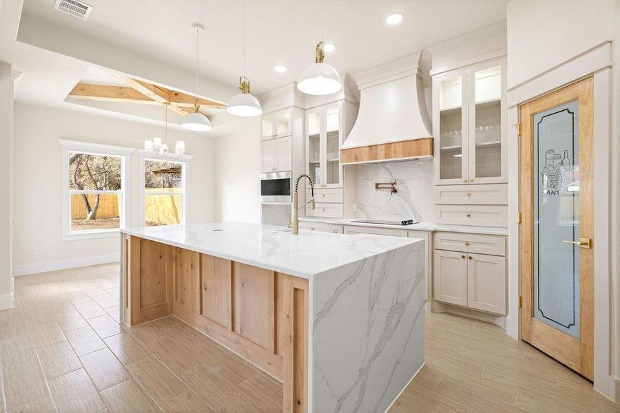 Kitchen with black electric stovetop, custom exhaust hood, visible vents, decorative backsplash, and a sink