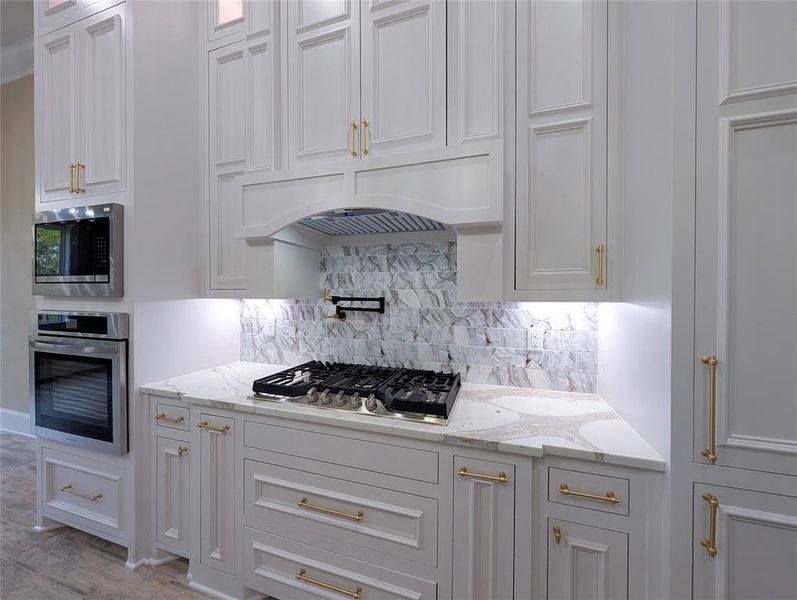Kitchen featuring light stone counters, stainless steel appliances, decorative backsplash, and white cabinetry