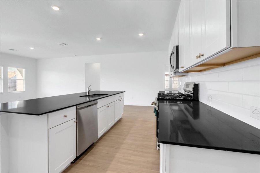 Kitchen with appliances with stainless steel finishes, white cabinetry, light wood finished floors, a center island with sink, and recessed lighting