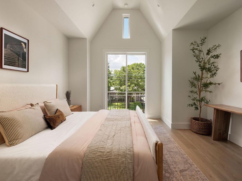 An airy bedroom with a high vaulted ceiling opens to a private balcony overlooking verdant landscaping.
