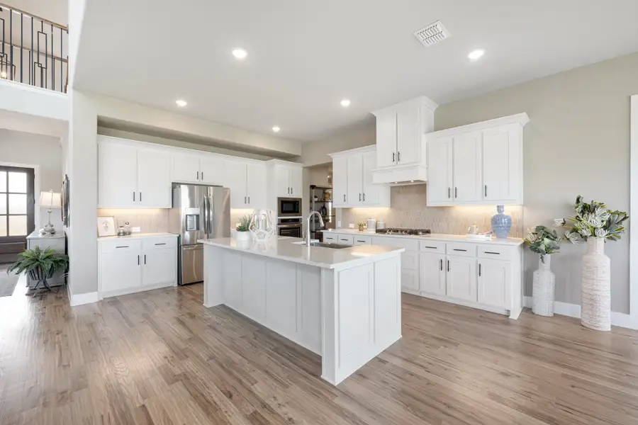 Open kitchen with white cabinets, large center island, stainless steel appliances, and light wood floors