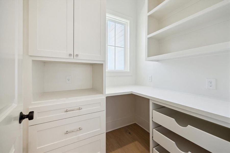 A beautifully designed pantry maximizes storage and organization. Custom cabinetry and built-in open shelving provide space for dry goods, kitchen appliances, and more, while drawers offer additional storage solutions. A well-placed window fills the space with natural light, creating a bright and functional environment. Sleek countertops offer a convenient surface for prep work or small appliances, making this pantry both practical and stylish for everyday use.