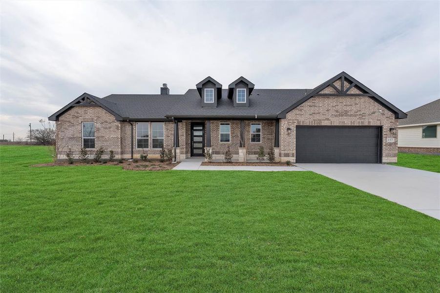 View of front facade featuring brick siding, a front lawn, driveway, an attached garage, and a shingled roof