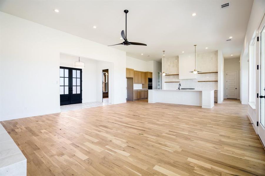 Unfurnished living room featuring ceiling fan, light hardwood / wood-style flooring, a healthy amount of sunlight, and french doors