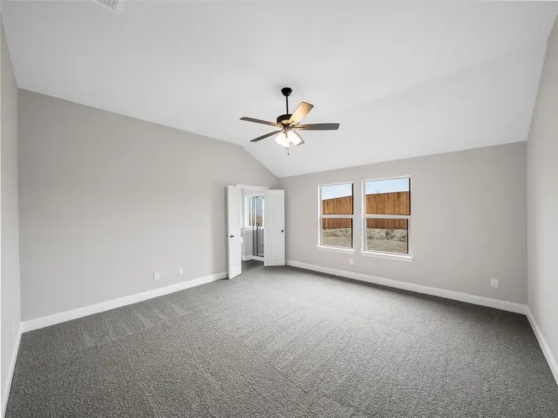 Carpeted empty room featuring ceiling fan, lofted ceiling, and baseboards