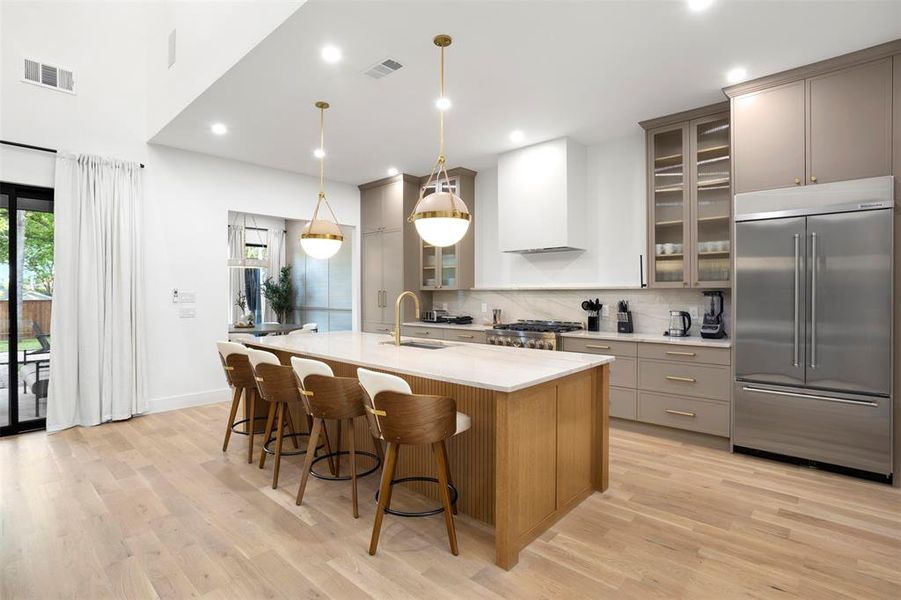 Spacious kitchen featuring a large central island with seating, integrated stainless steel appliances, light wood-finish flooring, and a vaulted ceiling