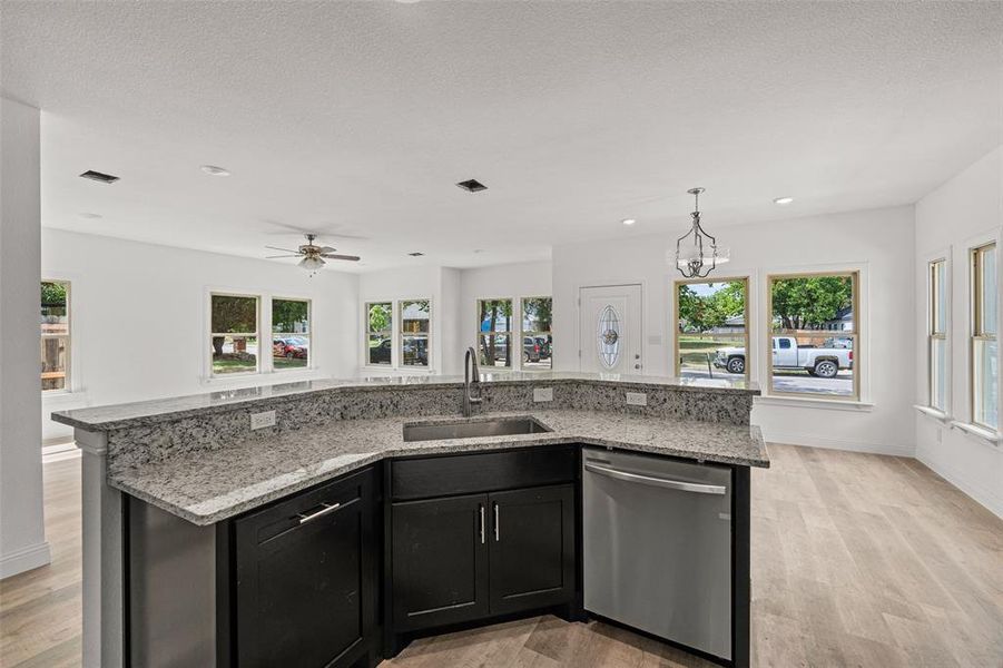 Kitchen featuring light hardwood / wood-style flooring, a kitchen island with sink, stainless steel dishwasher, decorative light fixtures, and sink