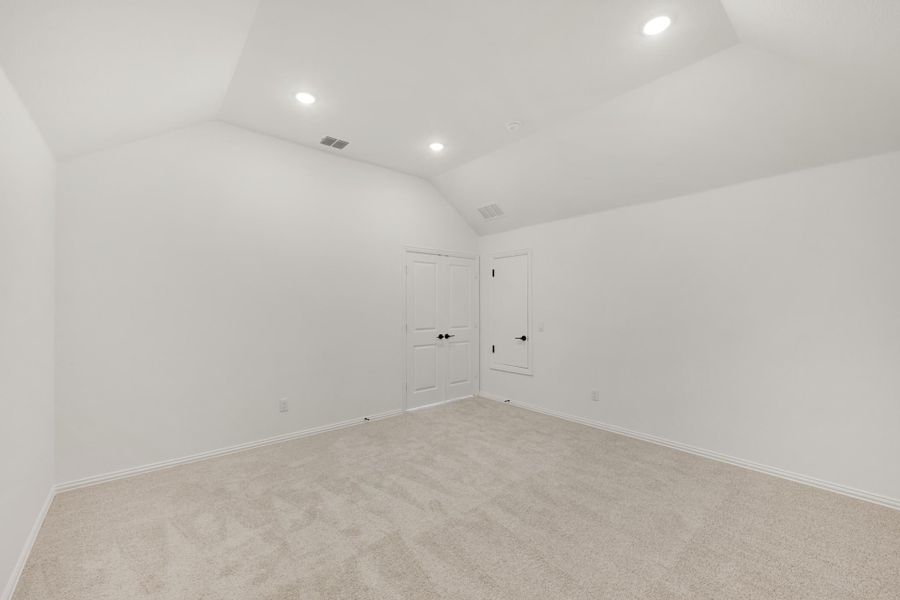 Empty bedroom with vaulted ceiling, carpet flooring, recessed lighting, and two white doors