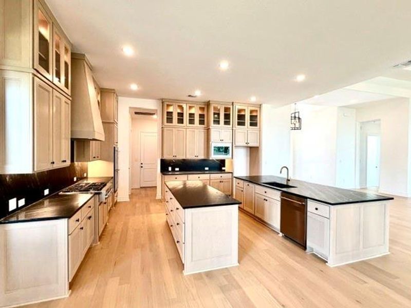 An open concept kitchen features two generous islands, sleek dark countertops, and ample cabinetry for culinary pursuits. An open concept kitchen features two generous islands, sleek dark countertops, and ample cabinetry for culinary pursuits.