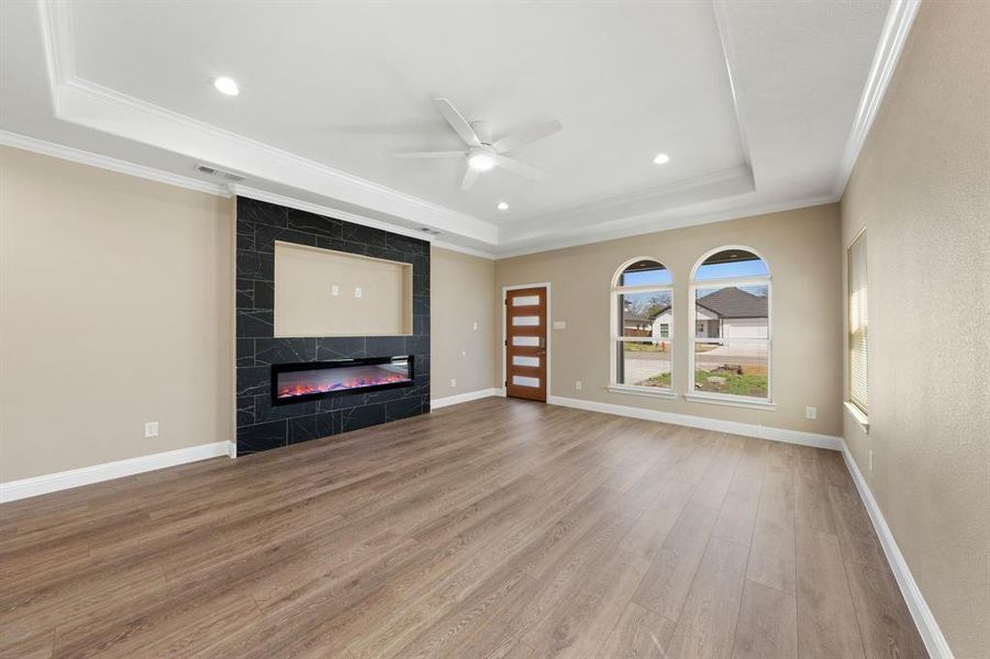 Unfurnished living room featuring baseboards, a raised ceiling, ornamental molding, wood finished floors, and a high end fireplace