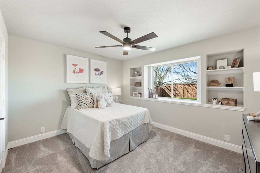 Child's bedroom with built-in shelves, ceiling fan, carpet flooring, and a large window