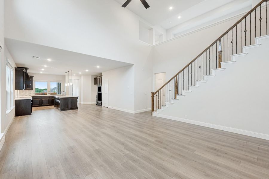Open living area with high ceilings, hardwood floors, staircase with iron balusters, and kitchen with dark cabinets in background