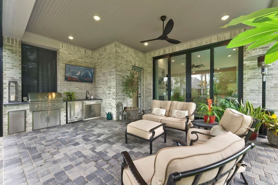 A closer look at this true entertaining patio with paved flooring, a full built-in outdoor kitchen, TV area, and upgraded wood plank ceiling. It extends the main living space outdoors and creates an inviting setting for year-round gatherings.