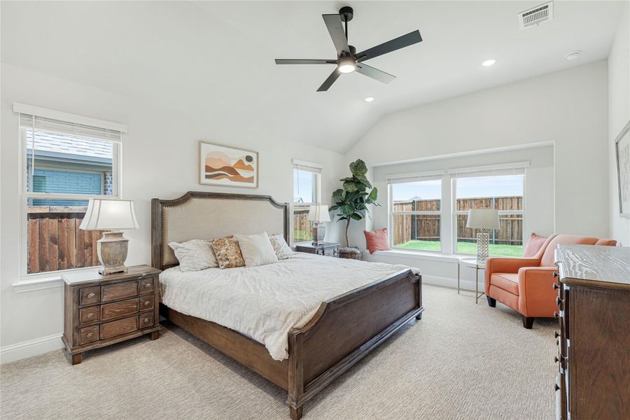 Spacious master bedroom with vaulted ceiling, ceiling fan, wood bed frame, and carpet flooring