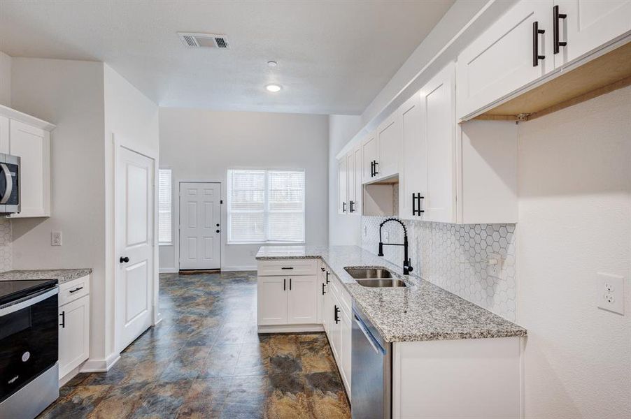 Kitchen featuring appliances with stainless steel finishes, sink, backsplash, and white cabinetry