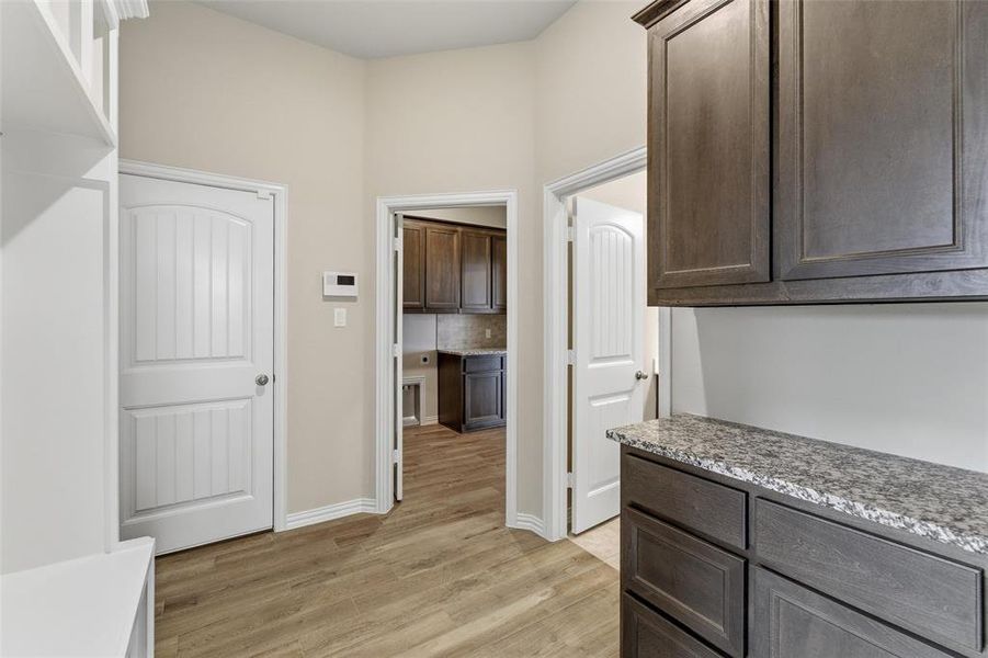 Kitchen featuring dark wood finish cabinetry, light wood finished floors, light stone countertops, and decorative backsplash