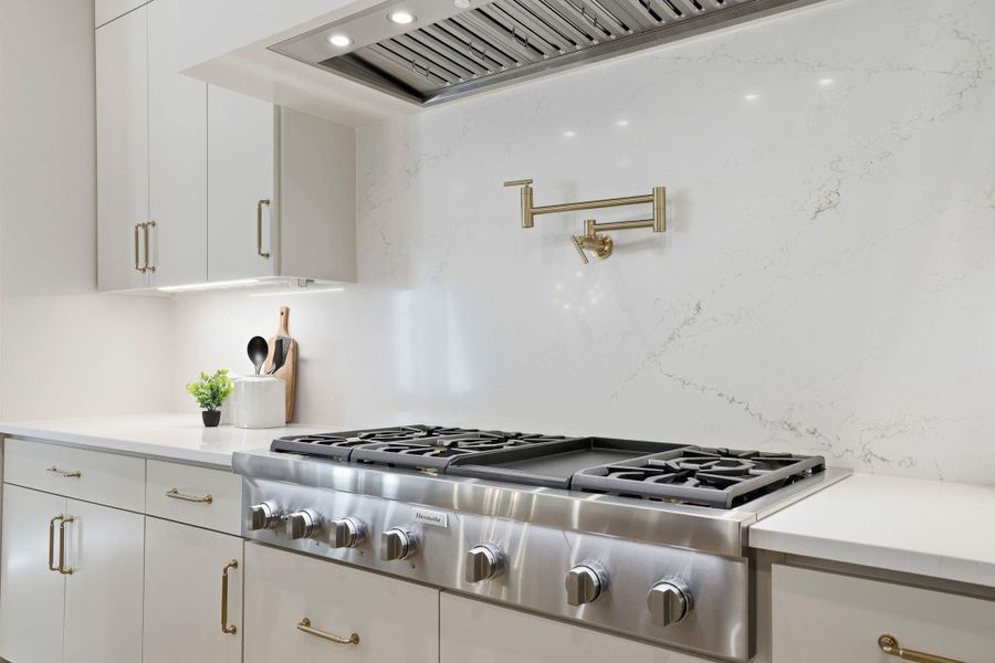 Kitchen featuring stainless steel gas cooktop, white cabinetry, and light stone countertops